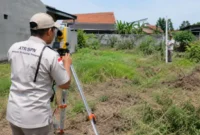 Petugas melakukan pengukuran bidang tanah sebagai bagian dari layanan Pengukuran Terjadwal untuk pendaftaran tanah pertama kali (Ilustrasi AI: sisipublik.com))